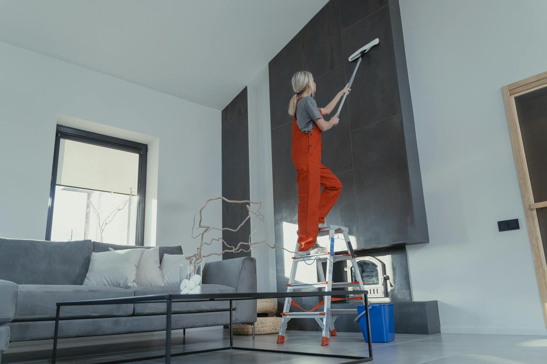 NYC Maid cleaner in red overalls on a ladder cleaning a high wall in a Manhattan apartment — Post-Construction Cleanup in Grymes Hill, Staten Island