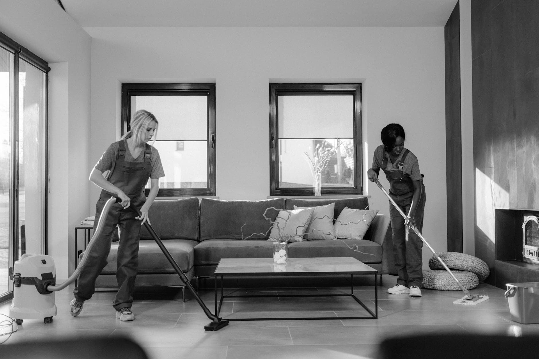 Two NYC Maid cleaners in work uniforms using a vacuum and mop in a modern Manhattan living room — hiring in Eastchester, Westchester