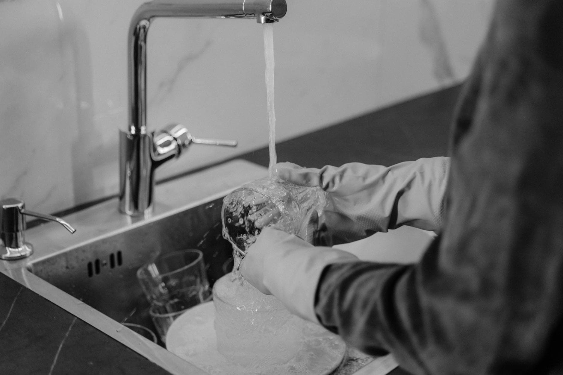 NYC kitchen cleaning service washing dishes under running water at the sink — cleaning services in Bronx River, Bronx