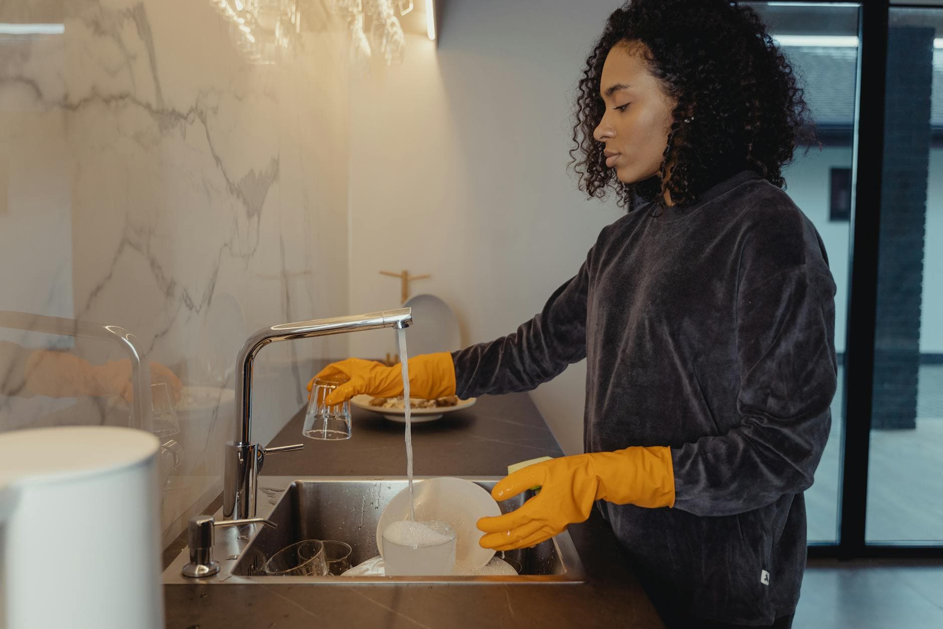 NYC maid wearing rubber gloves washing dishes in a modern Manhattan kitchen — Deep Cleaning in Chelsea, Staten Island